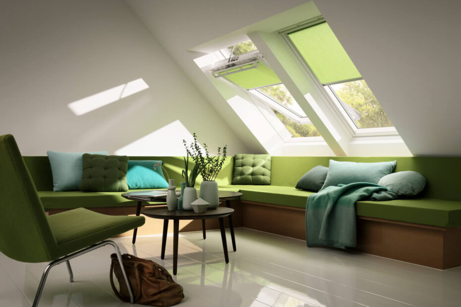 A cozy, modern attic living space with green cushions, a sofa, and Velux skylight windows letting in ample sunlight.
