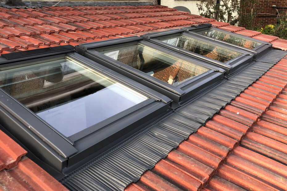 The image shows a close-up of a slanted red-tiled roof with four dormer Velux windows installed.