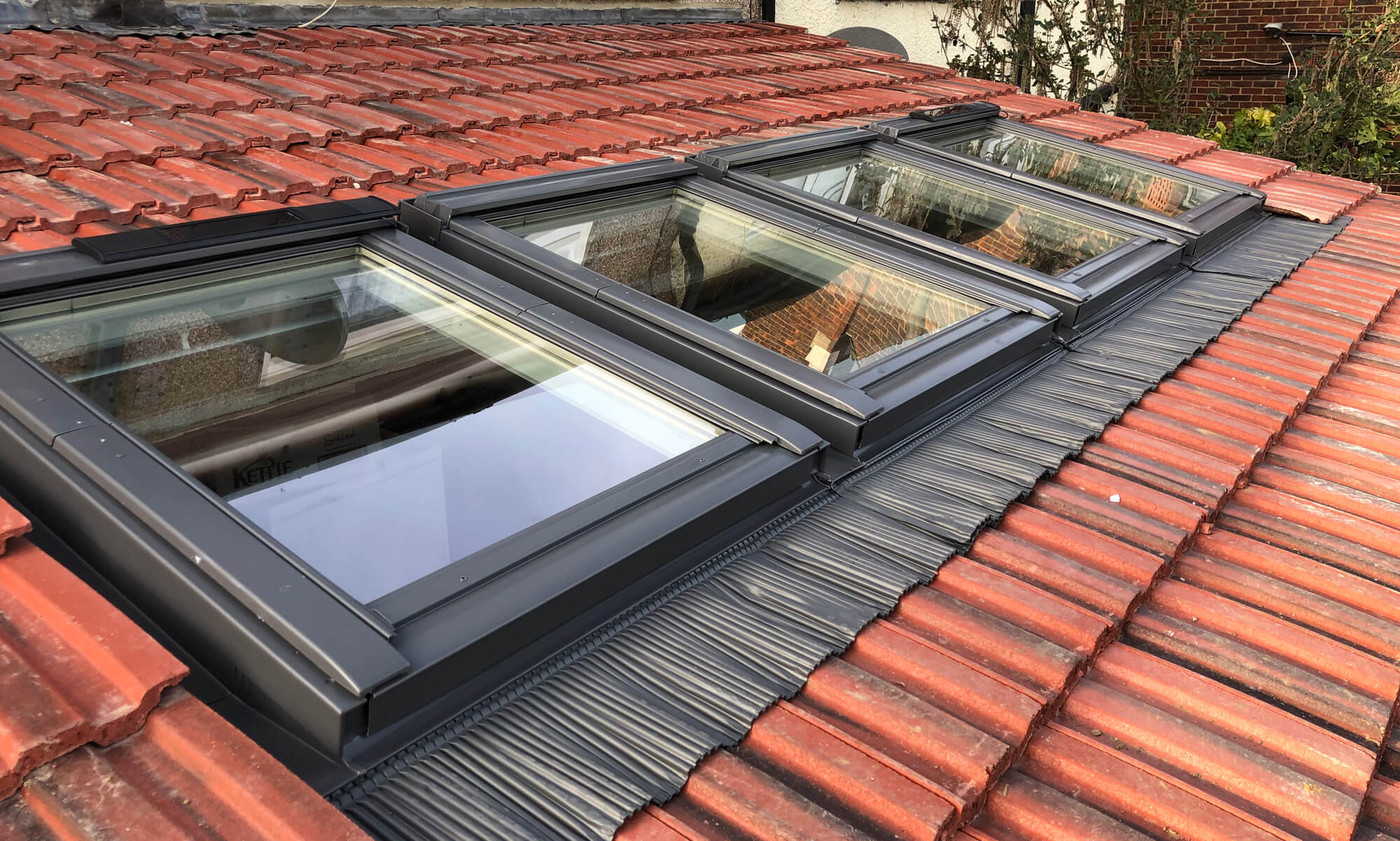 The image shows a close-up of a slanted red-tiled roof with four dormer Velux windows installed.