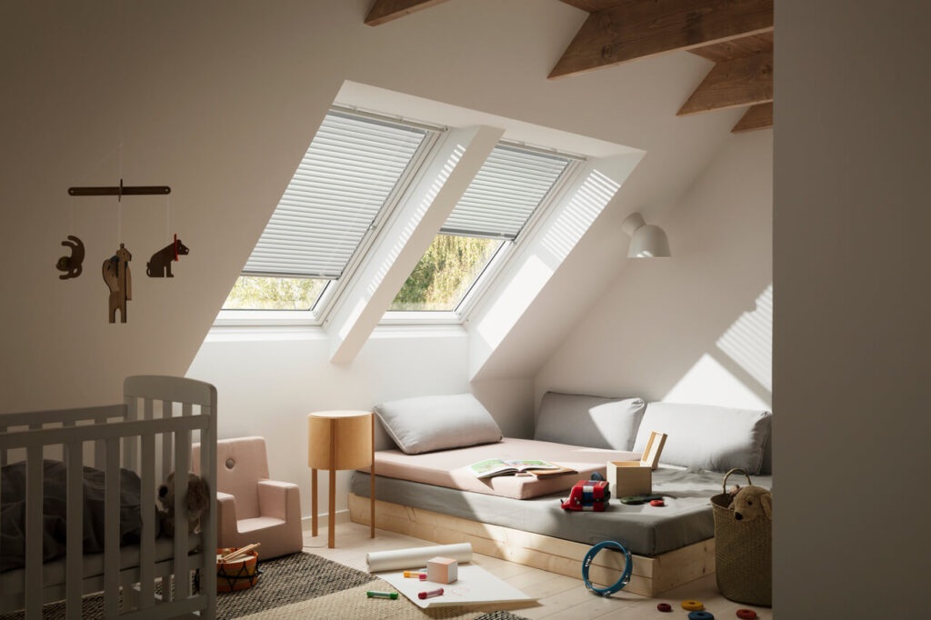 A cozy attic nursery room with a crib, toys, a daybed, and Velux skylights filtering in soft natural light.