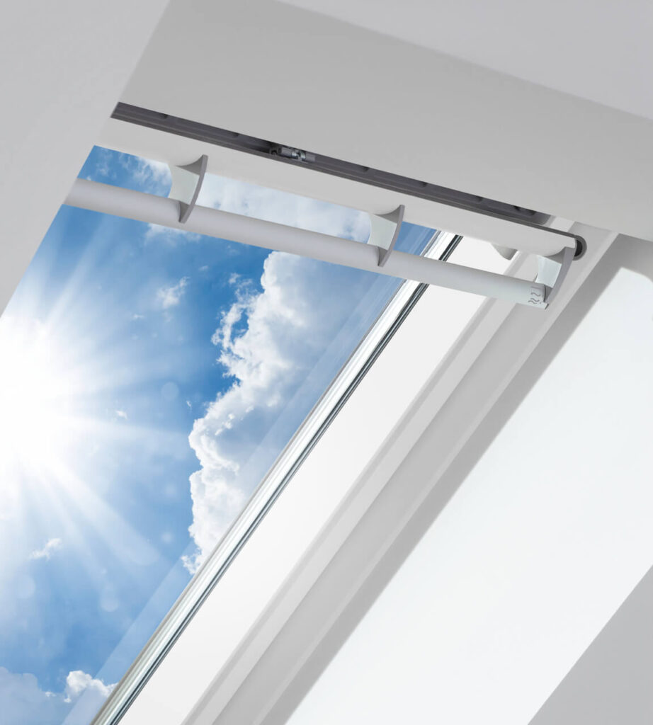 A Velux window on a sloped ceiling is open, showing blue sky and clouds.