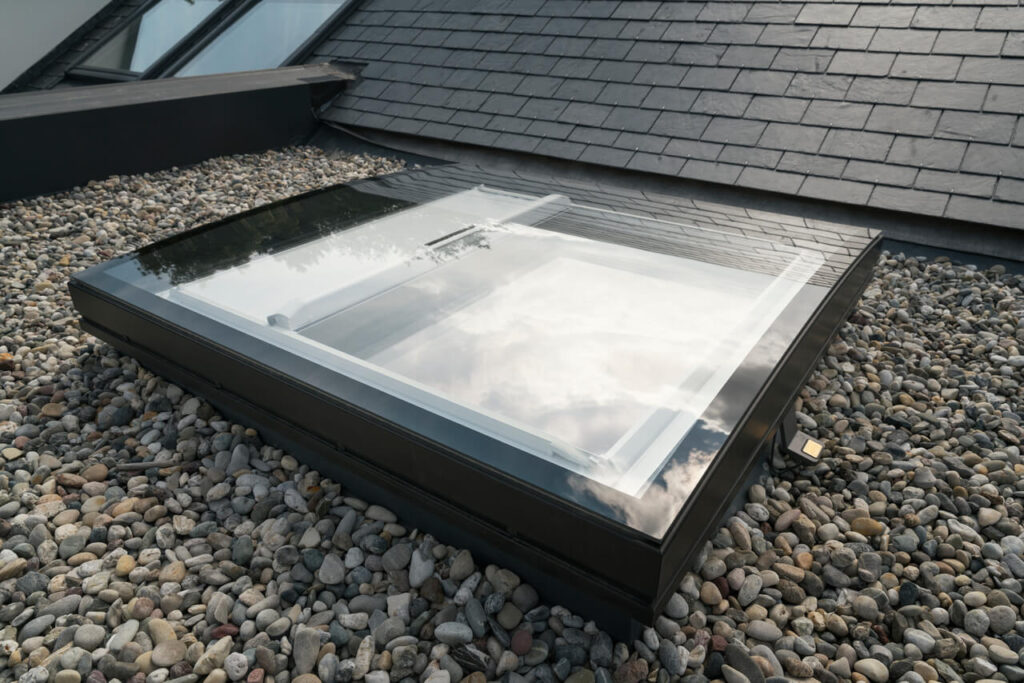 A modern Velux skylight window installed on a flat section of a gravel-covered roof.