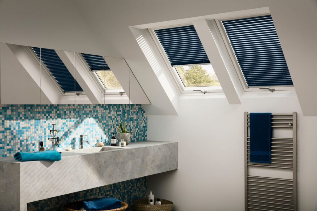 A modern attic bathroom with Velux skylights, blue blinds, and a mosaic tile backsplash.