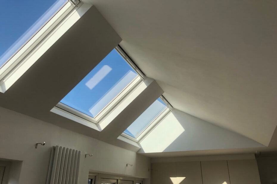 The image shows a modern interior with a sloped ceiling featuring Velux skylights that let in abundant natural light.